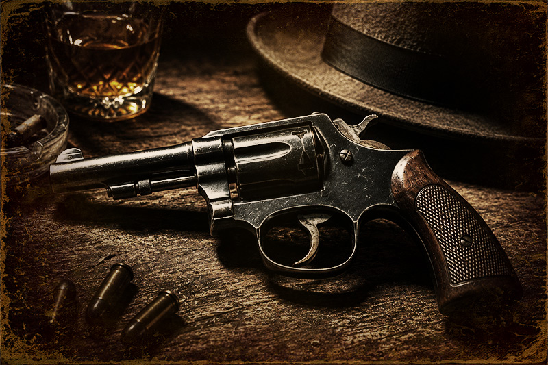 Vintage revolver resting on a worn wooden table beside loose cartridges, a whiskey glass, an ashtray, and a fedora hat.