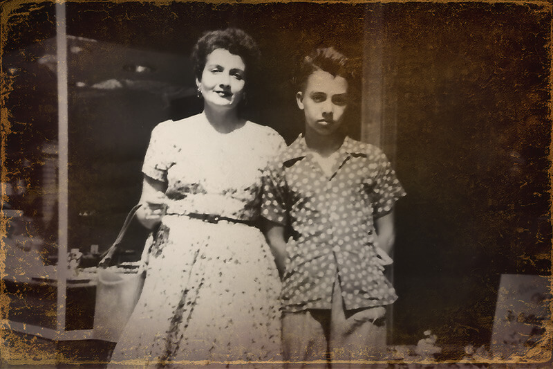 Vintage-style photograph of a young Vince Ciacci standing beside his mother outdoors.