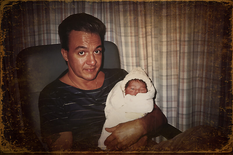 Stylized vintage portrait of Vince Ciacci holding his sleeping newborn daughter while looking at the camera.